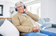 © Sharne/peopleimages.com - Portrait, home and old man with tablet, headphones and smile with connection, streaming music and radio. Senior person, technology and pensioner with headset, listening to audio and sound on a couch