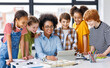© JenkoAtaman - Cheerful  schoolkids  with teacher looking at tablet screen and study the scheme of assembly of robots during collective school work    .