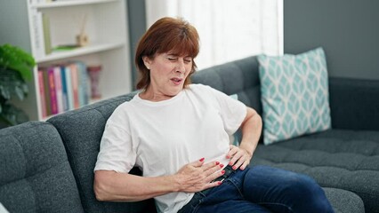 Canvas Print - Middle age woman suffering for stomach ache sitting on sofa home