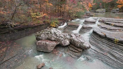 Wall Mural - Multiple waterfalls flow over rock cascade from a stream in the mountains during autumn with fall colored forest tree leaves  
