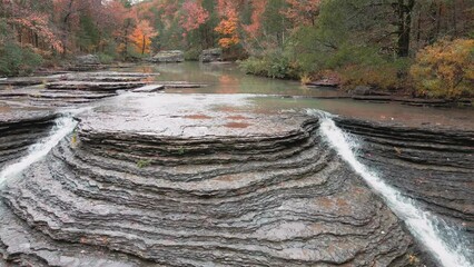 Wall Mural - Multiple waterfalls flow over rock cascade from a creek in the mountains during autumn with fall colored forest tree leaves  