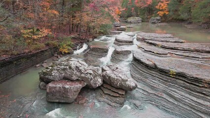Wall Mural - Multiple waterfalls cascade over rock river bed in the mountains during autumn with fall colored forest tree leaves  