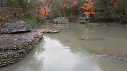 Wall Mural - Multiple waterfalls flow over rock cascade in the mountains during autumn with fall colored forest tree leaves via aerial drone capture   