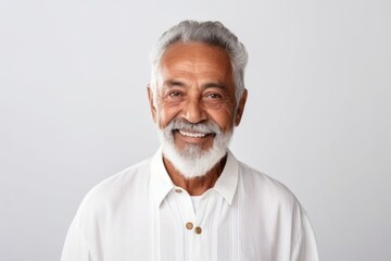 Medium shot portrait of a Brazilian man in his 70s in a white background wearing a simple tunic
