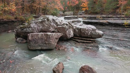 Wall Mural - Multiple waterfalls flow over rock cascade in the mountains during autumn with fall colored forest tree leaves via low aerial capture    