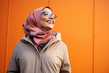 Wall Mural - Portrait of beautiful young muslim woman wearing hijab and coat on orange background