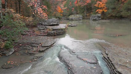 Wall Mural - Multiple waterfalls flow over rock cascade in the mountains during autumn with fall colored forest tree leaves via slow aerial view 