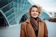 © Leon Waltz - Portrait of smiling businesswoman in trench coat looking at camera outdoors