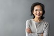 © Eber Braun - Portrait of a smiling mature Asian woman with crossed arms standing against grey background