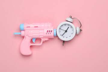 Plastic gun with alarm clock on pink background. Creative layout. Minimalism