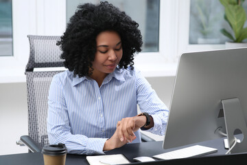 Poster - Young woman checking time on watch at table in office