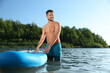 © New Africa - Man standing near SUP board in river water on sunny day