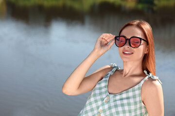 Wall Mural - Beautiful woman in sunglasses near river, space for text