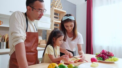 Wall Mural - Happy family with father, mother and daughter in kitchen while mother chop apple fruit together at home, happiness mom, dad and child with bonding and relation, lifestyles and nutrition concept.