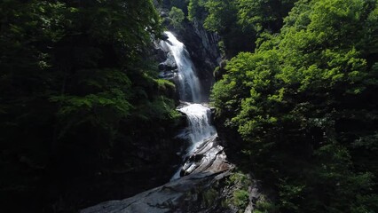 Wall Mural - Aerial video of a small waterfall in the dark forest on a sunny day