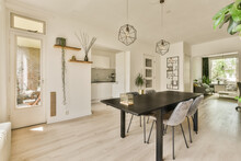 A Dining Room With White Walls And Wood Flooring In The Center Of The Room, There Is A Large Black Table Surrounded By