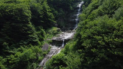 Wall Mural - Aerial video of a small waterfall in the dark forest on a sunny day