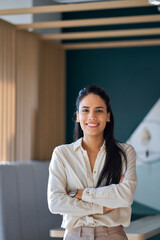 Wall Mural - Confident happy professional young latin business woman company employee, lady executive manager, smiling female worker or entrepreneur looking at camera standing in modern office, vertical portrait.