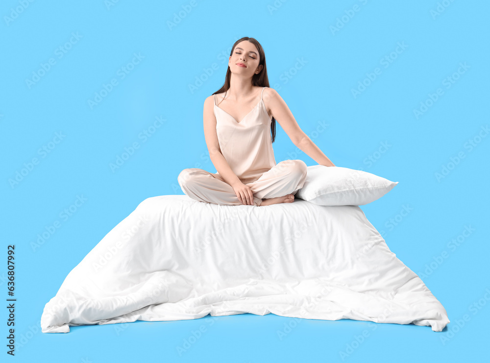 Young woman with soft pillow and blanket on blue background
