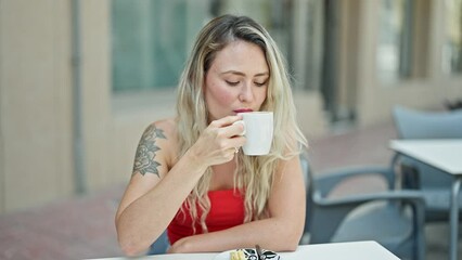 Poster - Young blonde woman drinking coffee sitting on table smiling at coffee shop terrace