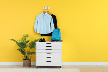 Wall Mural - Stylish school uniform hanging on yellow wall with chest of drawers in room