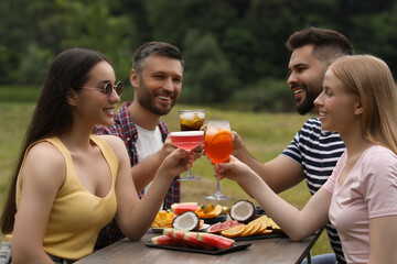 Wall Mural - Happy friends clinking glasses with cocktails at table outdoors