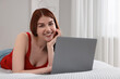 © New Africa - Happy woman with laptop on bed in bedroom