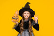 © Юлия Дьякова - Portrait of an angry little witch holding an evil pumpkin head. A child in a sorceress costume. Children's carnival on Halloween. Yellow bright isolated background.