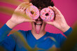 Funny attractive guy eats donuts. Pink background.