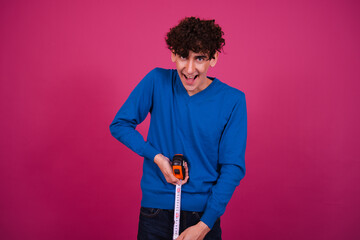 Funny attractive guy measures the length. Pink background.