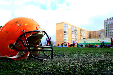 A large orange american football helmet stands close up on the green grass of the stadium