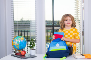 Fototapete - School child 7-8 years old with book go back to school. Little student doing homework at home, puts school supplies in a backpack. Preparation for school.