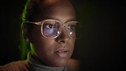 Close-up of the reflection of the computer screen on the glasses of a business woman working with a laptop in a dark room. Concept of computer network security and hacking in the Internet space