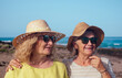 © luciano - Family couple of senior and middle aged women embraced standing outdoors at sea wearing sunglasses and hats. Vacation, freedom, friendship concept. Horizon over water