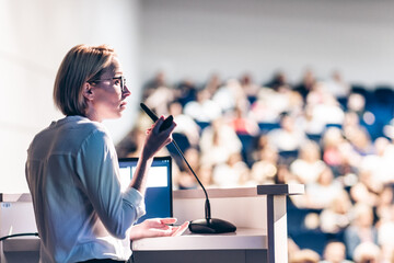 Wall Mural - Female speaker giving a talk on corporate business conference. Unrecognizable people in audience at conference hall. Business and Entrepreneurship event