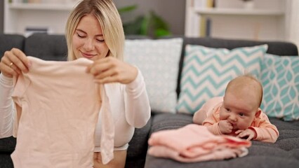 Sticker - Mother and daughter holding baby clothes sitting together at home