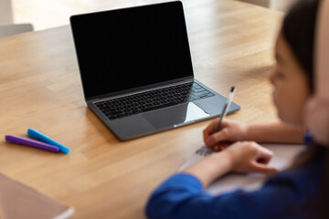 Schoolgirl using laptop with empty screen taking notes indoor