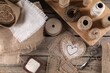 Pieces of burlap fabric, spools of twine and different sewing tools on wooden table, flat lay