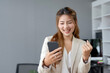 © amnaj - Happy young Asian business woman Successful excited raised hands rejoicing with smartphone.