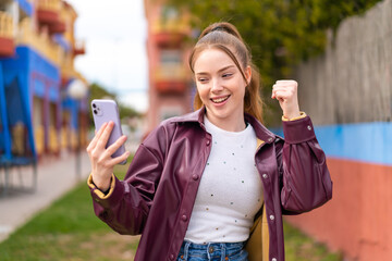 Poster - Young pretty girl using mobile phone at outdoors celebrating a victory