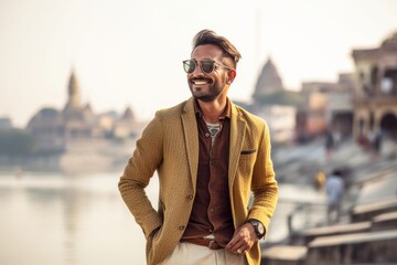 Wall Mural - Handsome bearded Indian man in yellow jacket and sunglasses standing on the river bank