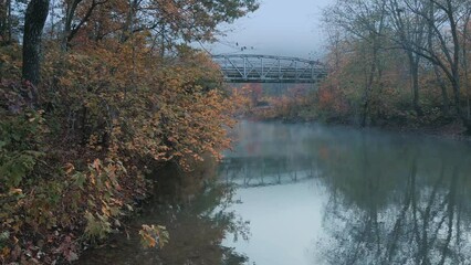 Wall Mural - Rustic old steel bridge over autumn green river with fog in mountain country scenic location 