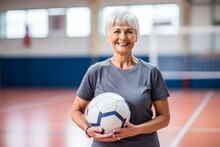 Portrait Of Smiling Senior Woman Holding Soccer Ball In Sports Hall At Home