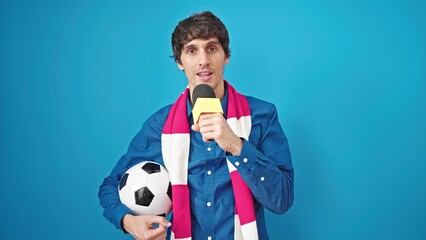 Poster - Young hispanic man soccer reporter working using microphone holding football ball over isolated blue background