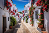 Fototapeta Fototapeta uliczki - Picturesque narrow street in Spanish city old town. Typical traditional whitewashed houses with blooming plants, flowers, cobbled street in a small cozy town in Spain