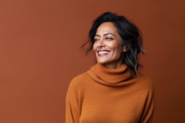 Wall Mural - Portrait of a smiling young woman in sweater posing on brown background