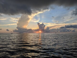 Wall Mural - Stunning sunset over a tranquil ocean, with clouds in the sky and small boats dotting the horizon