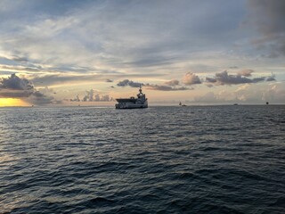 Canvas Print - Large ship sailing peacefully through the open waters of the sea at sunset with wispy clouds