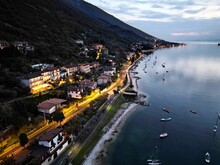 Illuminated Coastal Townscape With A Harbor Lined With Boats On Lake Garda At Dusk