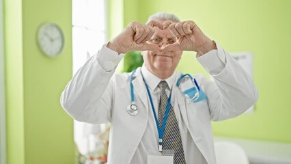 Canvas Print - Middle age grey-haired man doctor smiling doing heart gesture with hands at clinic